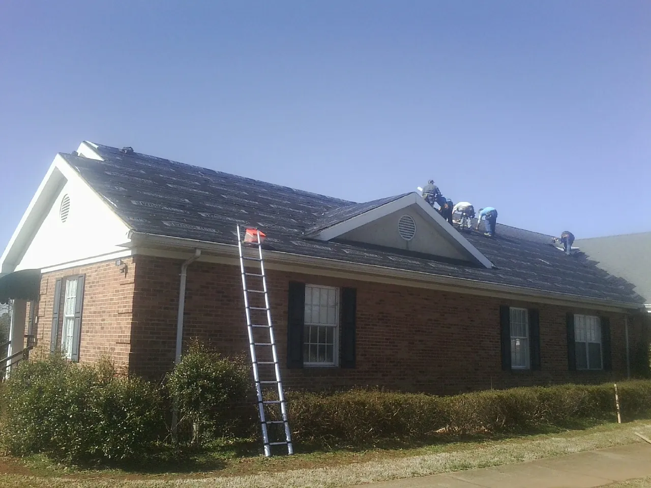 Crew tearing shingles off a brick ranch roof with a ladder set — Emergency Roof Repair work by our crew in Norwood Young America