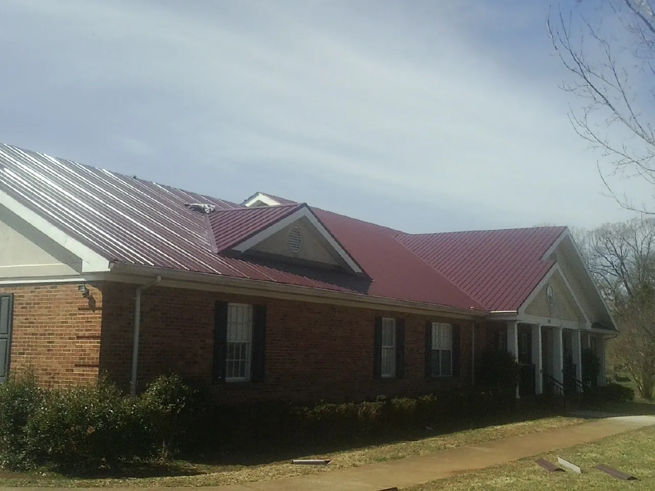 Red metal roof with gabled entries on a long brick building, from a Hail Damage Roof Repair job in Norwood Young America