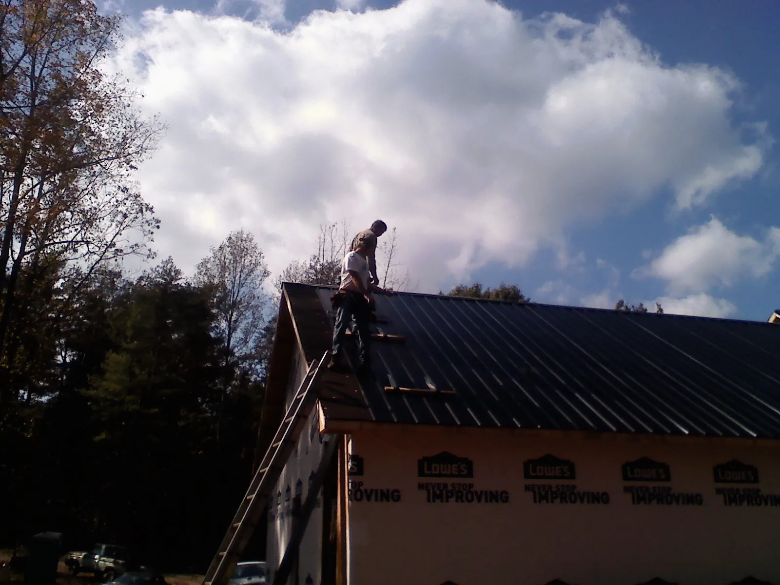 Roofer fastening dark metal panels high against a cloudy sky in Norwood Young America