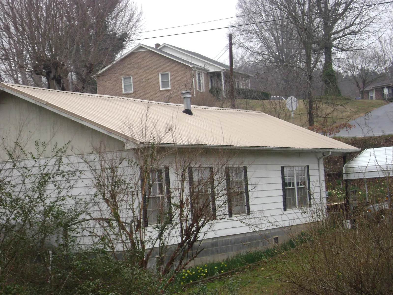 Tan metal roof on a white sided house set into a hillside — Commercial Roofing by Roofing Brothers in Norwood Young America